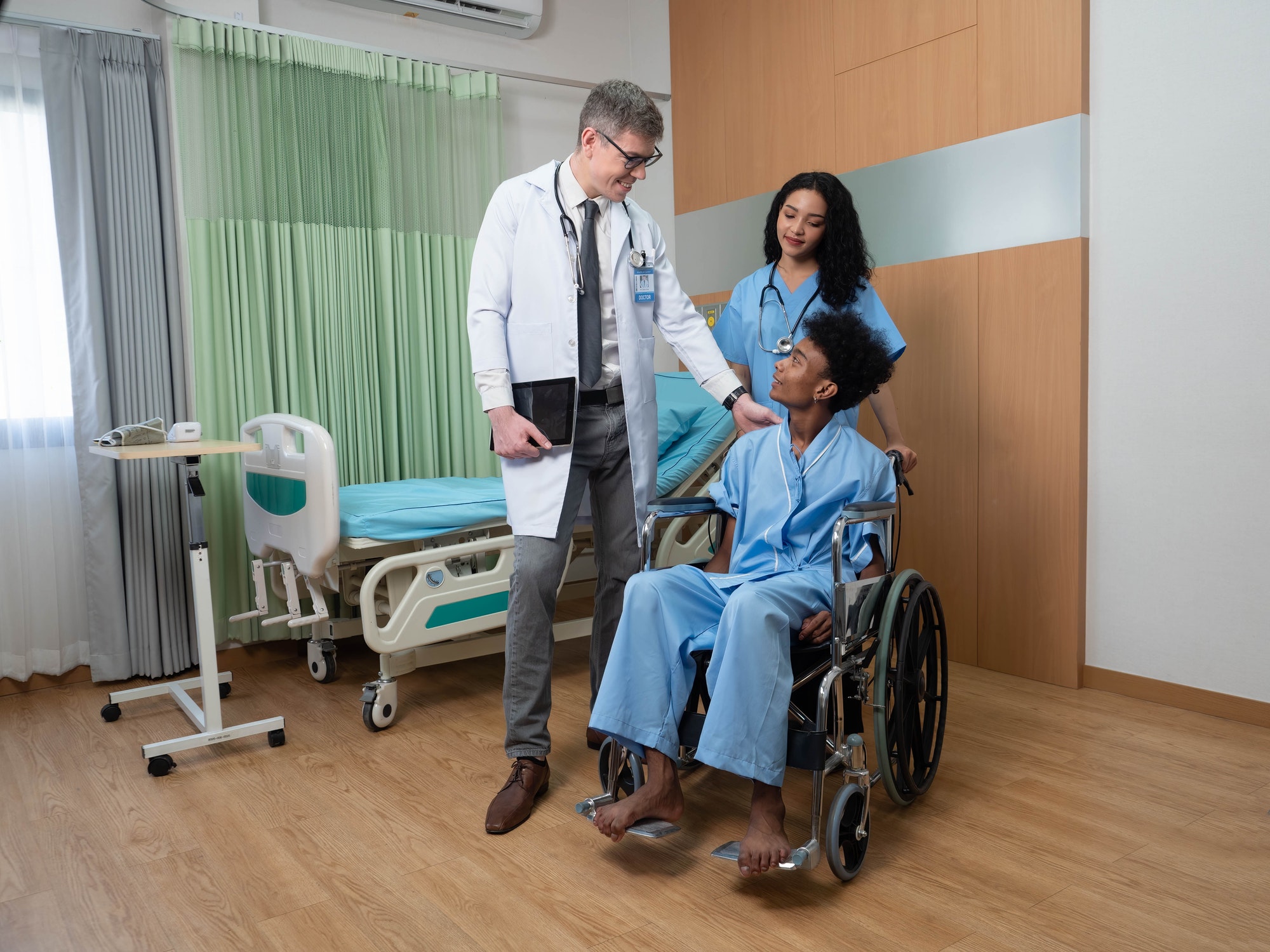 At hospital patient sitting on wheel chair nurse doctor congrats him for discharge from hospital